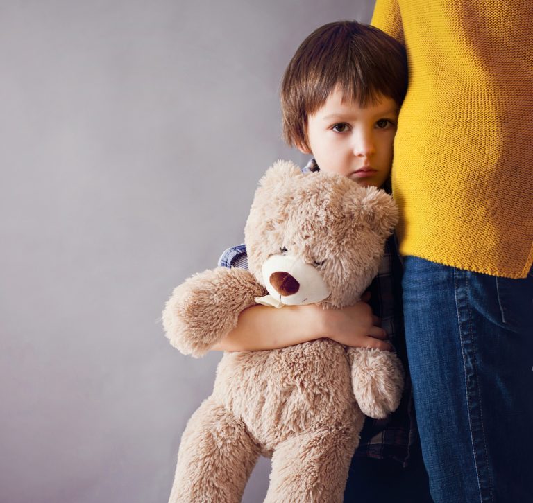 Young boy holding teddy bear and snuggling next to his mother